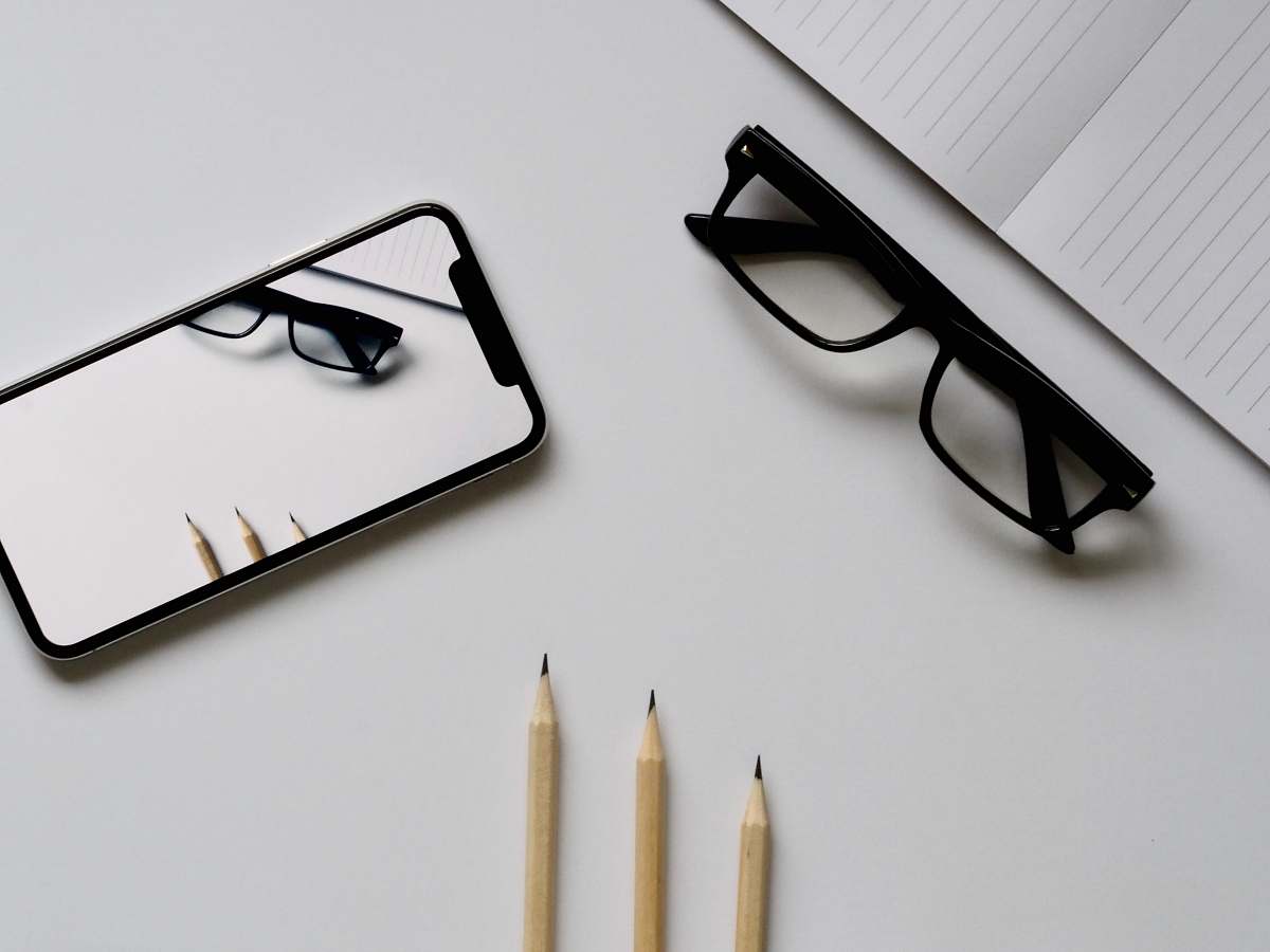 mobile phone eyeglasses; silver iPhone X; three pencils; notebook flat lay photography pencil